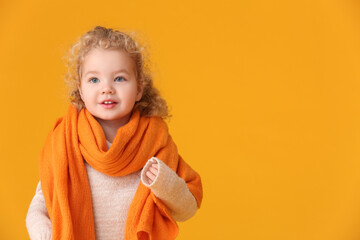 Cute little girl with warm scarf on color background