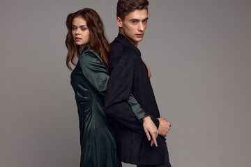 A man and a woman in love in evening suits stand with their backs to each other on a gray background