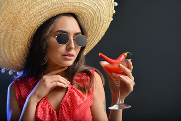 Beautiful young woman in sombrero hat and with spicy cocktail on dark background