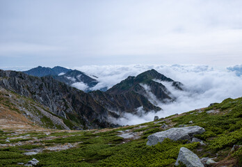 Naklejka na ściany i meble View of Kiso Mountains Range engulfed in thick clouds in the background with rock formations on grassland in the foreground in early autumn at Senjojiki Cirque in Nagano Prefecture, Japan.