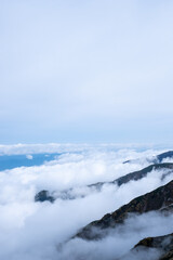 View of rocky mountain range and valley engulfed in clouds on the horizon in early autumn at Senjojiki Cirque in Nagano Prefecture, Japan.