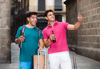 Two men are walking with beer and taking selfie near sights in Barcelona