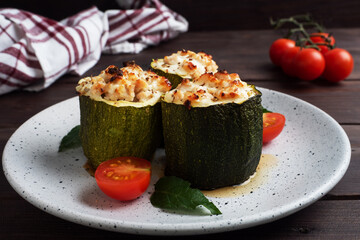 Baked stuffed zucchini columns with minced chicken and vegetables on a plate. Dark wooden background. Copy space.