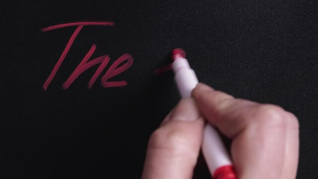 Woman's hand writes the word the end with a red felt-tip pen on a black board. Concept of the finale