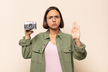 young latin woman looking serious, stern, displeased and angry showing open palm making stop gesture