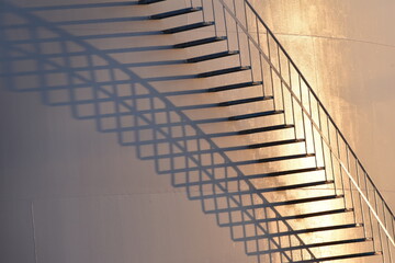 Closeup of large oil tank, detail of stairs and railing.  Diagonal and curving shadows of stairs at sunset.