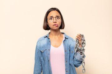 young latin woman looking puzzled and confused, biting lip with a nervous gesture, not knowing the...