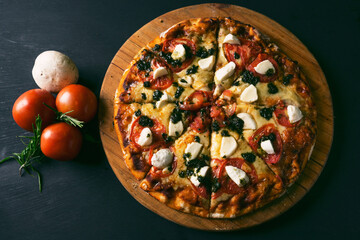top view Traditional italian pizza with green basil pesto sauce on a black rustic wooden background. Top view of hot pizza. With copy space for text.