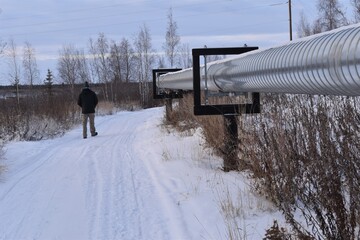 Man walking beside utilidors, above ground utility pipes in a northern Canadian town, with snow and...