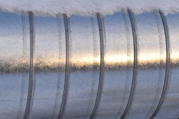 Horizontal aluminum pipe or conduit, above ground, with snow on top. Part of utilidor system.