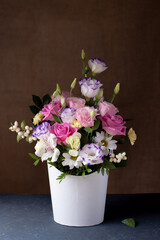 romantic bouquet of roses, daisies, lisianthus, chrysanthemums, unopened buds in a white round box, on a gray table and a background of burlap.