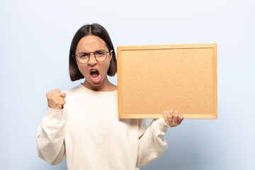 young latin woman shouting aggressively with an angry expression or with fists clenched celebrating...