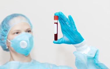 A female laboratory assistant (nurse) holds a test tube with a blood test in her hand and a place...