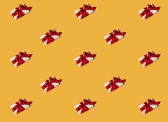 Gift pattern. Orange seamless background. Party decor. Long-distance present. Symmetrical composition of white boxes with red ribbon bows isolated on bright yellow.