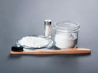 Zero waste concept for teeth cleaning. A bamboo toothbrush with a floss and toothpowder in the glass on the grey background.