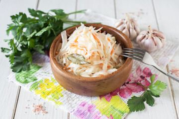 Pickled cabbage with carrots in a wooden plate on a white table
