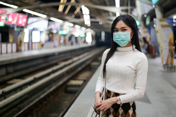Beautiful asia woman passenger wearing medical hygiene protective face mask infection from coronavirus covid-19 standing in lines waiting sky train on platform at night.