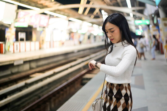 Beautiful Asia Woman Looking At Watch Standing In Lines Waiting Sky Train On Platform At Night.