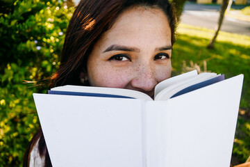 Woman with cute freckles smiling and hiding her face with a book