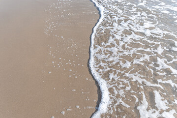 Fototapeta na wymiar Sparkling waves hitting the shore on the beach, sand beige background image.