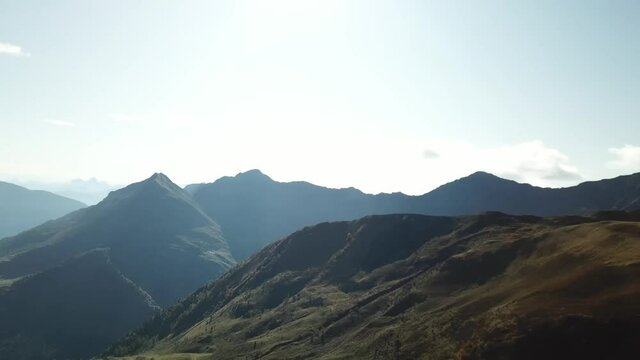 A panoramic drone shot of the Carnic mountain chain in Austrian Alps. Highest parts of the mountains are baren and stony, lower part are overgrown with moss. Lush green valley. Serenity 
