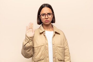 young latin woman looking serious, stern, displeased and angry showing open palm making stop gesture