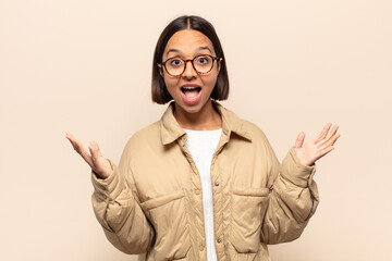 young latin woman feeling happy, excited, surprised or shocked, smiling and astonished at something...