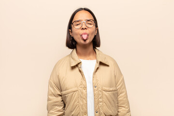 young latin woman with cheerful, carefree, rebellious attitude, joking and sticking tongue out,...