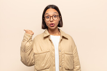 young latin woman looking astonished in disbelief, pointing at object on the side and saying wow,...