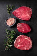 Meat cuts, top shot with salt and rosemary on a black background