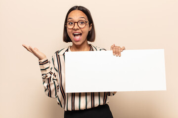 young latin woman feeling happy, excited, surprised or shocked, smiling and astonished at something...