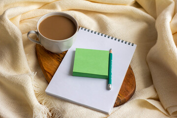 A Cup of coffee with milk and a Notepad with a pen on a light cozy blanket.