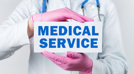 Cropped view of female doctor in a white coat and pink sterile gloves holding a card with words - medical service