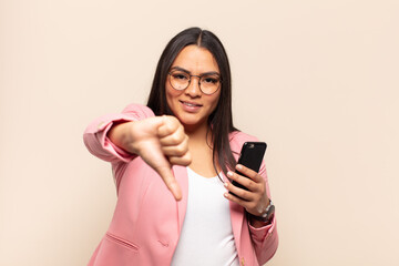young latin woman feeling cross, angry, annoyed, disappointed or displeased, showing thumbs down...