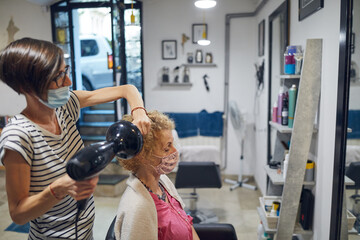 Fototapeta premium Hairdresser and customer in a salon with medical masks during virus pandemic. Working with safety mask.