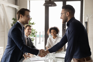 Happy multiracial businesspeople shake hands get acquainted greeting at meeting in office. Smiling...