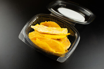 Small plastic box or casserole with slices of dried mango on black background.