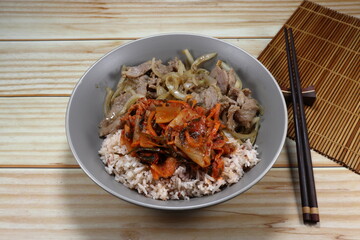 Fried and stirred pork with sliced onion in local style serving with cooked rice and kimchi (Korea spicy pickled mixed vegetable) on the plate.