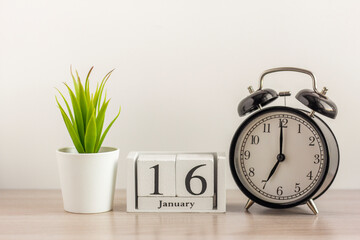 January 16 on a wooden calendar, next to a retro alarm clock and a succulent in a mini pot on a light table.One day in January.Winter day.A copy of the space.Workplace.