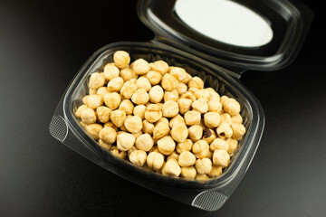 Peeled hazelnuts in a small plastic box or casserole on a black table.