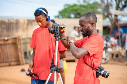 image of african guy, with camera and a colleague at background bit blurred - film production concept