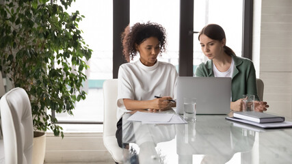 Wide banner panoramic view of female colleagues sit in boardroom look at laptop screen discus company project together. Women employees collaborate brainstorm using computer. Teamwork concept.