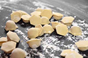 Dumplings, ravioli close-up, hexagonal shape of dough on a black table. Dusted with flour.