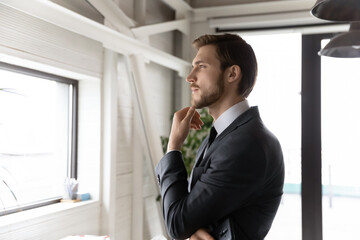 Pensive young Caucasian businessman look in window distance thinking pondering of future career success opportunities. Dreamy thoughtful male CEO or worker visualize or plan. Business vision concept.