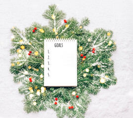 Fototapeta na wymiar Blank notebook for planning goals on New Year's green branches with lights