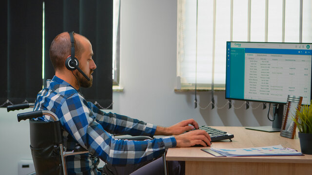 Handicapped disabled operator sitting in wheelchair making telemarketing in business office. Immobilized, disabled, paralysed freelancer working in financial corporate building using heatset