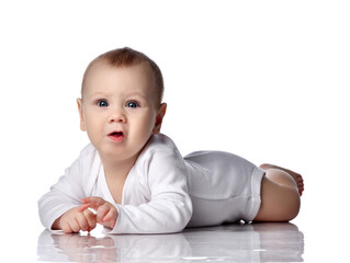 Distrustful barefooted infant baby boy toddler in diaper and bodysuit is lying on floor on his stomach, crawling watching new unknown over white background. Happy infancy and babyhood concept