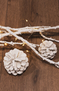 white fir-tree cones next to white branches in the dark are burning new year lights on a wooden background. christmas decor