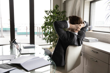 Back view of tired businessman sit lean in chair in office relax relieve negative emotions after...