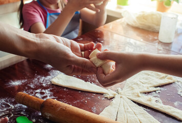 Mom and children prepare dough in the kitchen during self-isolation and quarantine. Hands of a woman, a boy and a girl in flour near the dough close-up. Concept of a happy family and cooking together